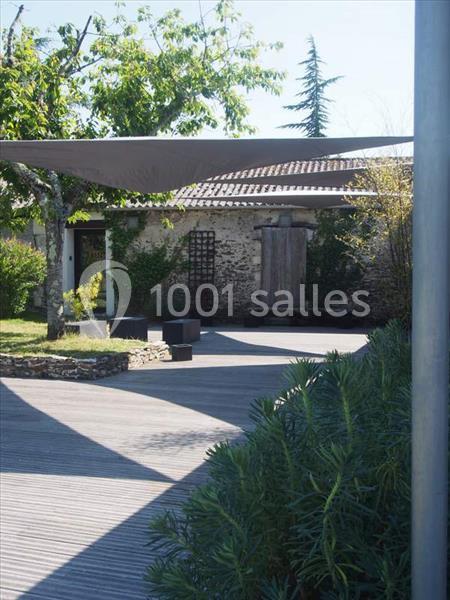 Cour extérieure avec terrasse en bois, voiles d'ombrage, végétation et façade en pierre ornée de verdure.