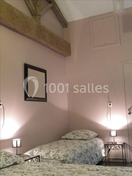 Deux lits simples avec linge à motifs floraux dans une chambre aux murs roses, éclairée par des lampes de chevet.