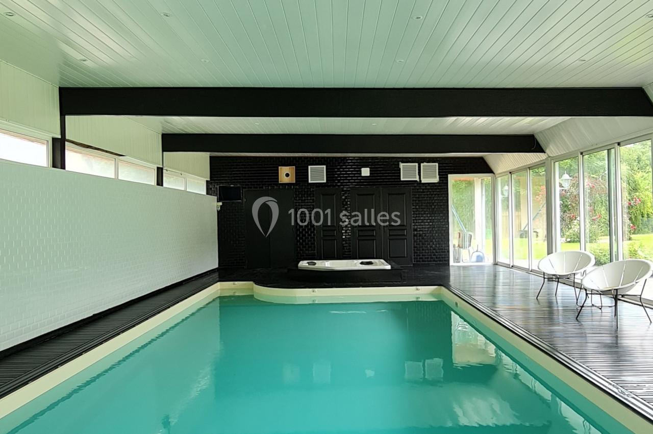 Piscine intérieure avec plafond en bois blanc, baies vitrées donnant sur un espace extérieur verdoyant.
