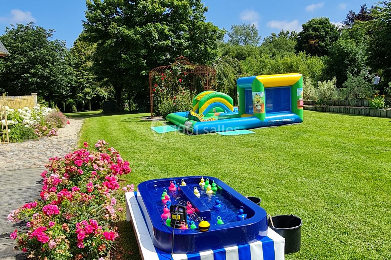 Structure gonflable colorée et jeu de pêche aux canards installés sur une pelouse entourée de fleurs et d'arbres.