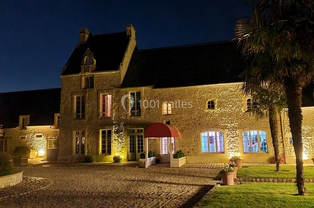 Façade d'un bâtiment en pierre éclairé la nuit, avec une entrée voûtée et des fenêtres illuminées.