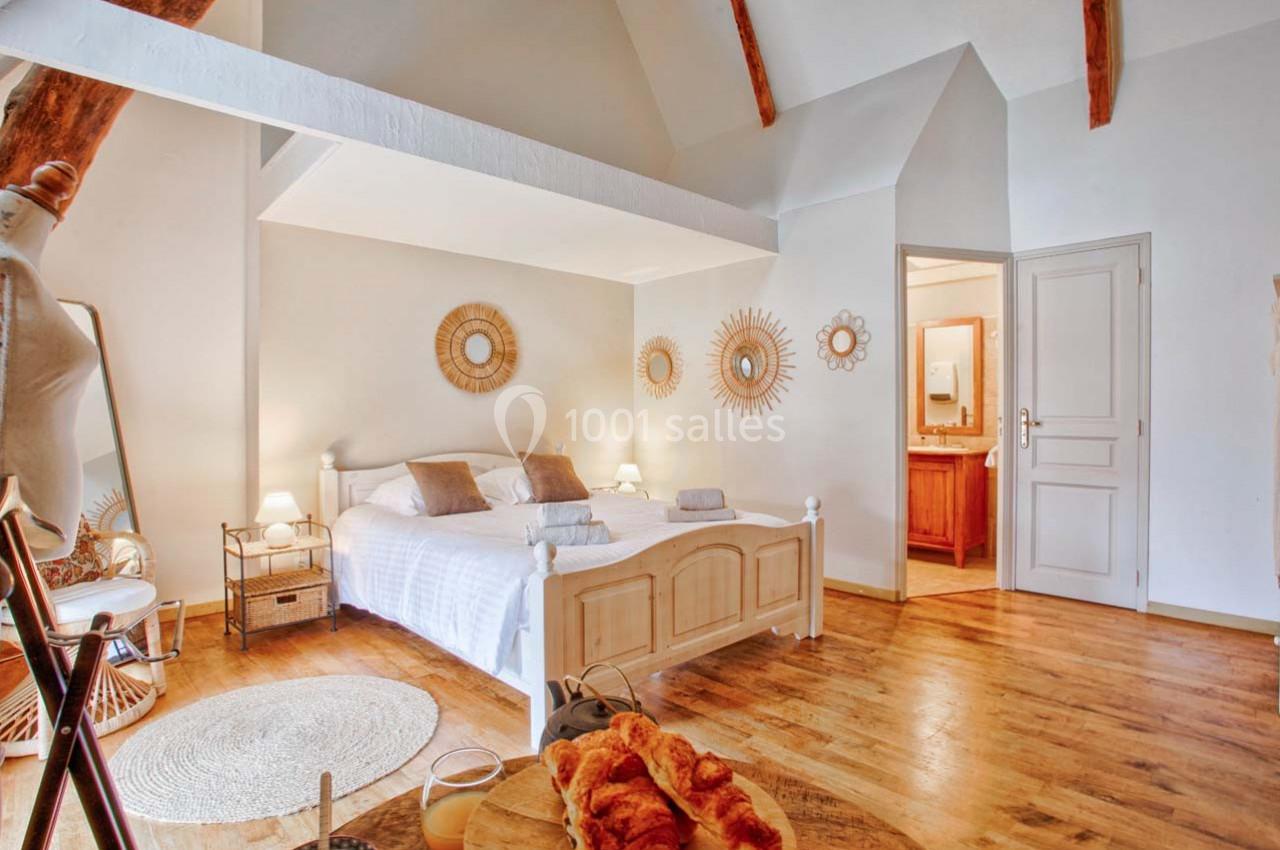 Chambre lumineuse avec lit double, décorations murales en rotin, parquet en bois et salle de bain attenante.