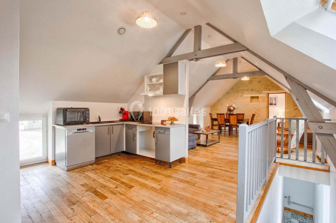 Cuisine ouverte sous combles avec poutres apparentes, parquet en bois et vue sur une salle à manger lumineuse.