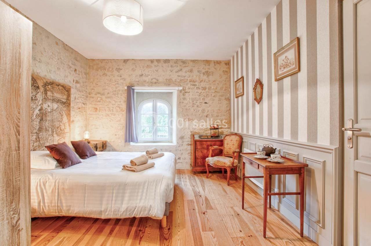 Chambre lumineuse avec murs en pierre et papier peint rayé, lit double, meubles anciens et parquet en bois clair.