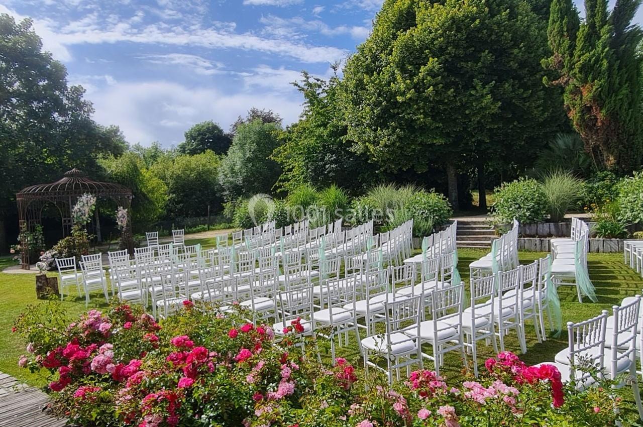 Chaises blanches alignées en extérieur, entourées de fleurs et de verdure, prêtes pour une cérémonie en plein air.