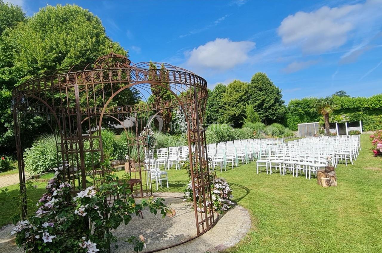 Structure métallique décorative entourée de fleurs dans un jardin, avec des rangées de chaises blanches en arrière-plan.