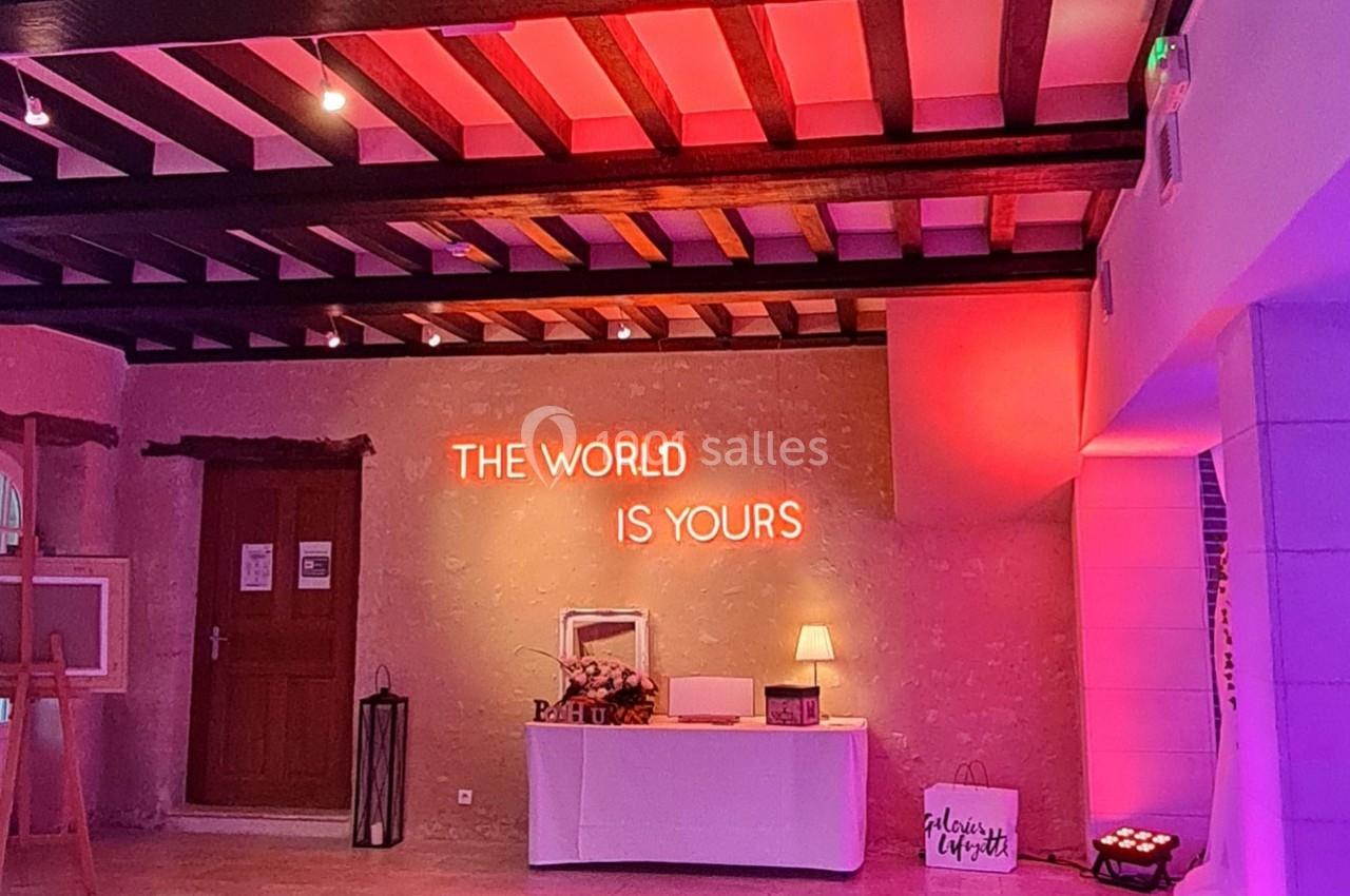 Salle éclairée par des lumières roses avec un néon ’The world is yours’ au mur, table décorative en dessous.