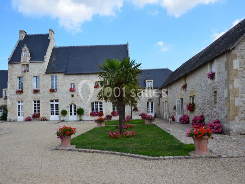 Cour d'une grande bâtisse en pierre avec des toits en ardoise, des fleurs colorées et un palmier au centre.