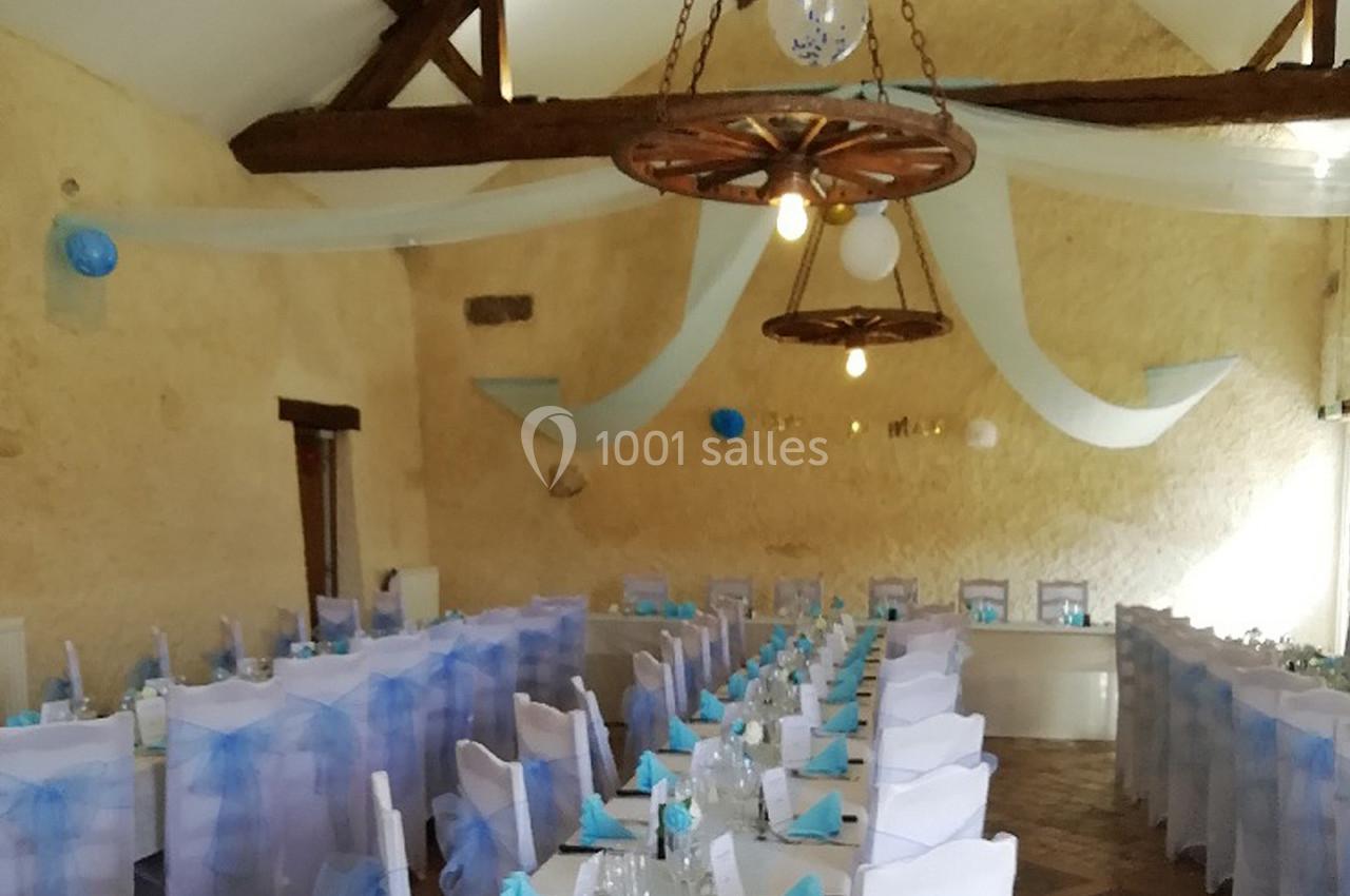 Salle de réception décorée avec des nappes blanches, des chaises ornées de voiles bleus et des guirlandes suspendues.