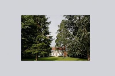 Grande maison blanche entourée d'arbres et d'une pelouse verte sous un ciel légèrement nuageux.