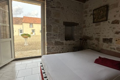 Chambre avec poutres apparentes, lit simple, armoire ancienne, bureau, chaise et fenêtre ouverte sur l'extérieur.