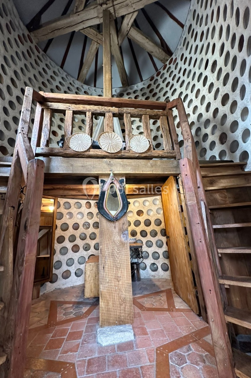 Intérieur d'un pigeonnier restauré avec murs en briques percées, charpente en bois et escalier menant à une mezzanine.
