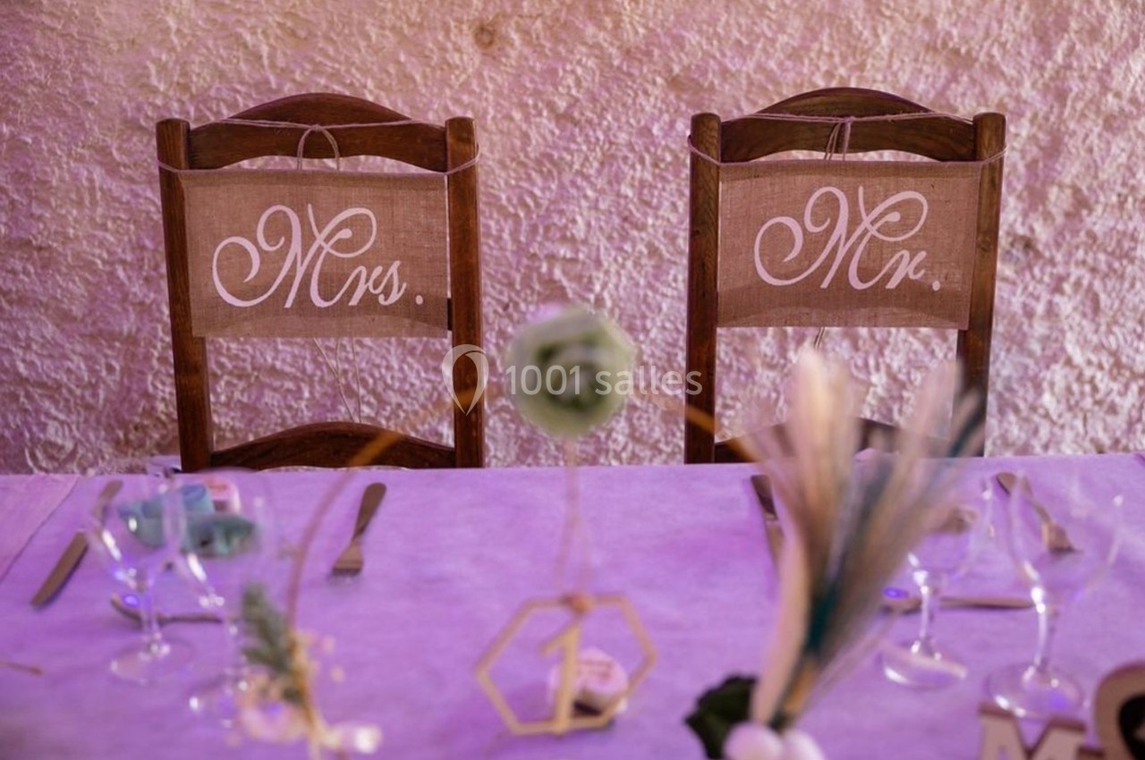 Deux chaises en bois décorées avec des panneaux ’Mrs.’ et ’Mr.’, placées derrière une table dressée pour un repas.