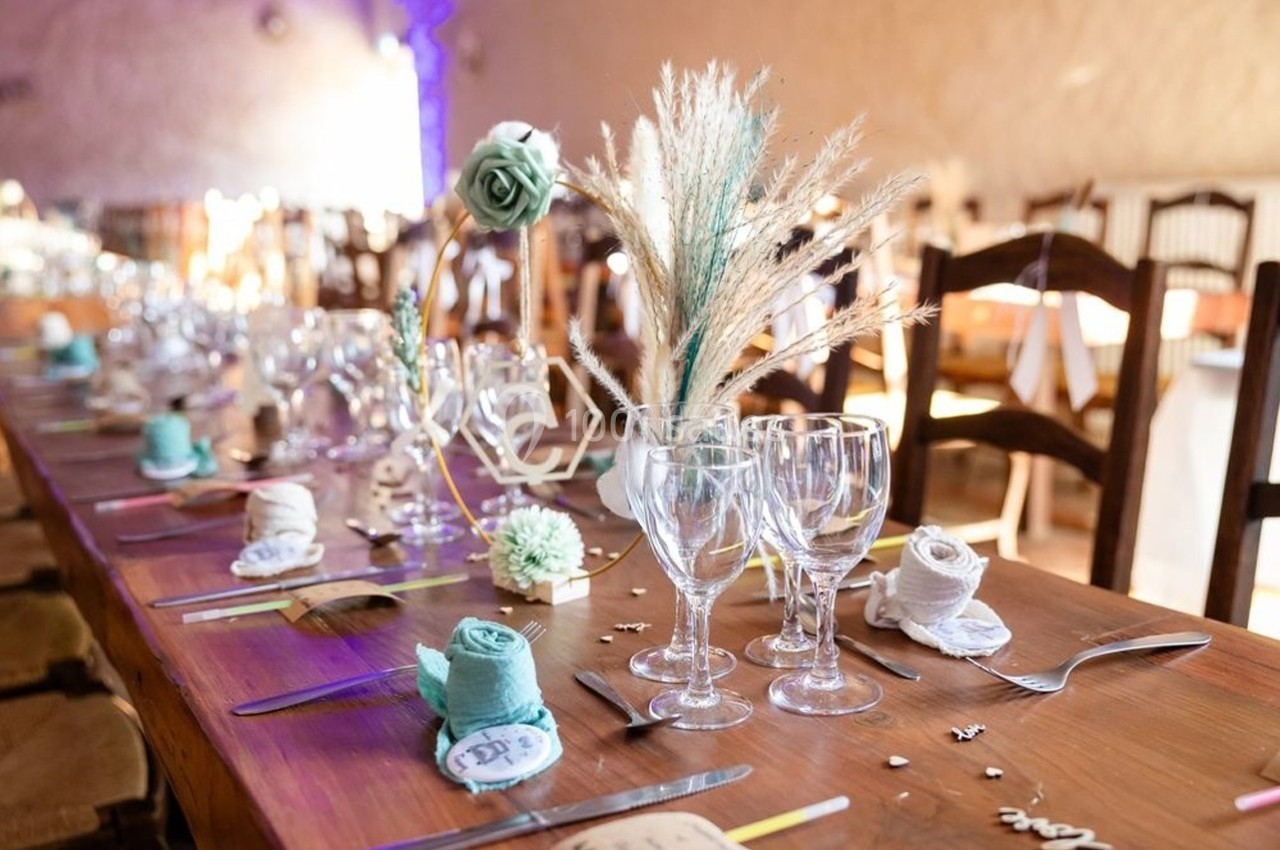 Table décorée pour un événement avec verres, couverts, serviettes pliées et ornements floraux dans une ambiance chaleureuse.