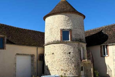 Cour pavée avec un puits en pierre au premier plan, entouré de bacs végétalisés, et bâtiments en arrière-plan.