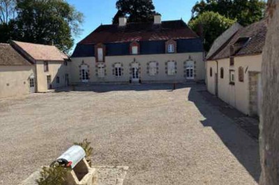 Cour pavée avec un puits en pierre au premier plan, entouré de bacs végétalisés, et bâtiments en arrière-plan.