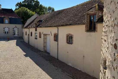 Cour pavée avec un puits en pierre au premier plan, entouré de bacs végétalisés, et bâtiments en arrière-plan.