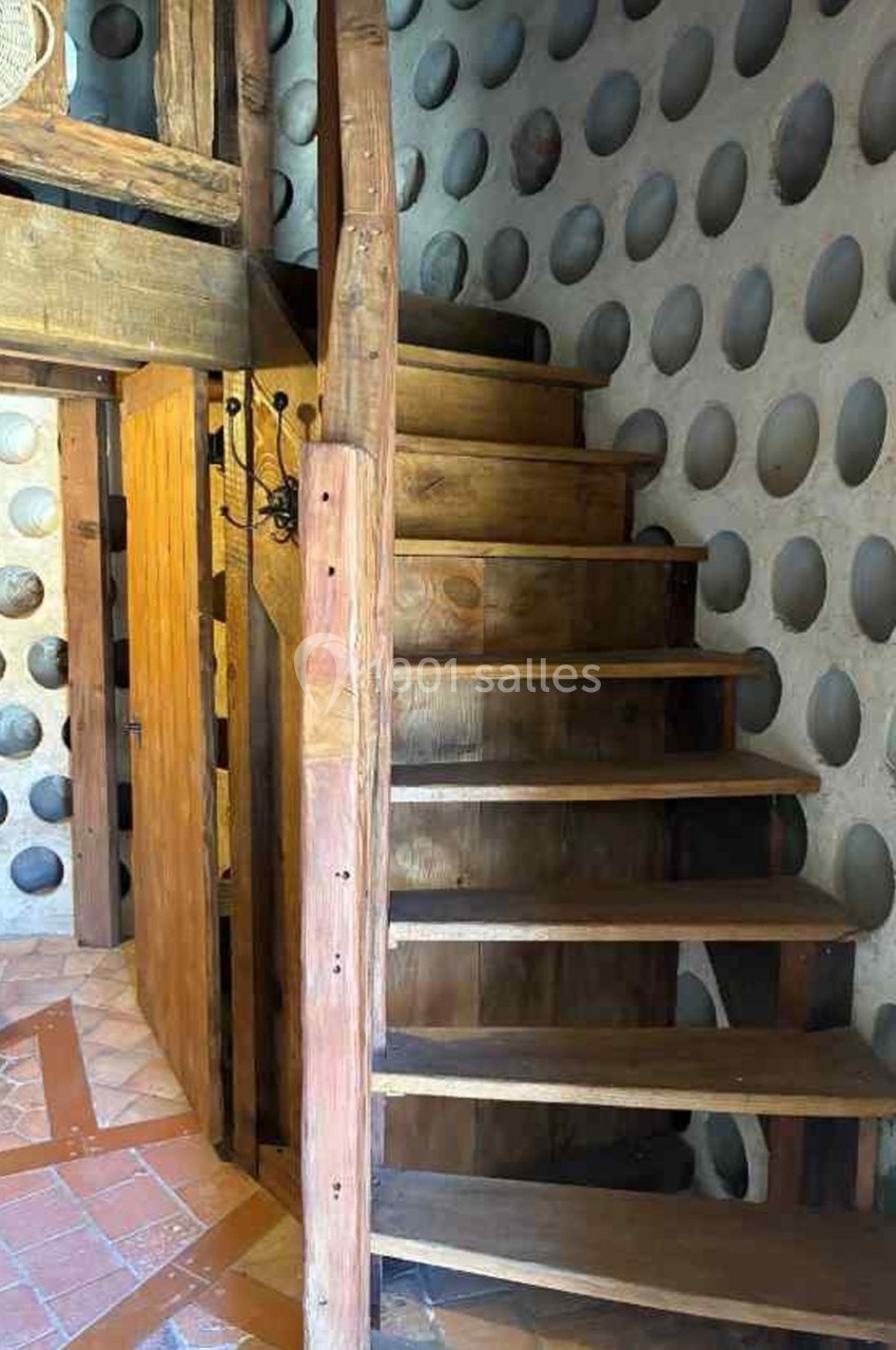 Escalier en bois avec rampe, dans une pièce aux murs ornés de motifs circulaires et sol en carreaux de terre cuite.