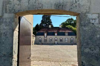Cour pavée avec un puits en pierre au premier plan, entouré de bacs végétalisés, et bâtiments en arrière-plan.