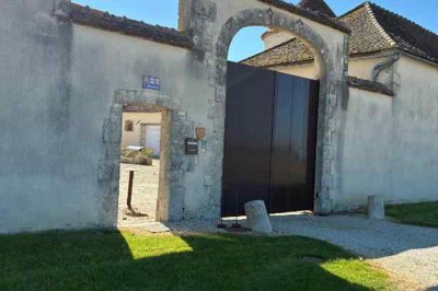 Cour pavée avec un puits en pierre au premier plan, entouré de bacs végétalisés, et bâtiments en arrière-plan.