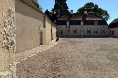 Cour pavée avec un puits en pierre au premier plan, entouré de bacs végétalisés, et bâtiments en arrière-plan.