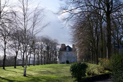 Champ verdoyant bordé d'arbres en automne, avec un grand bâtiment blanc visible à l'arrière-plan.
