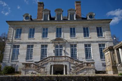 Champ verdoyant bordé d'arbres en automne, avec un grand bâtiment blanc visible à l'arrière-plan.