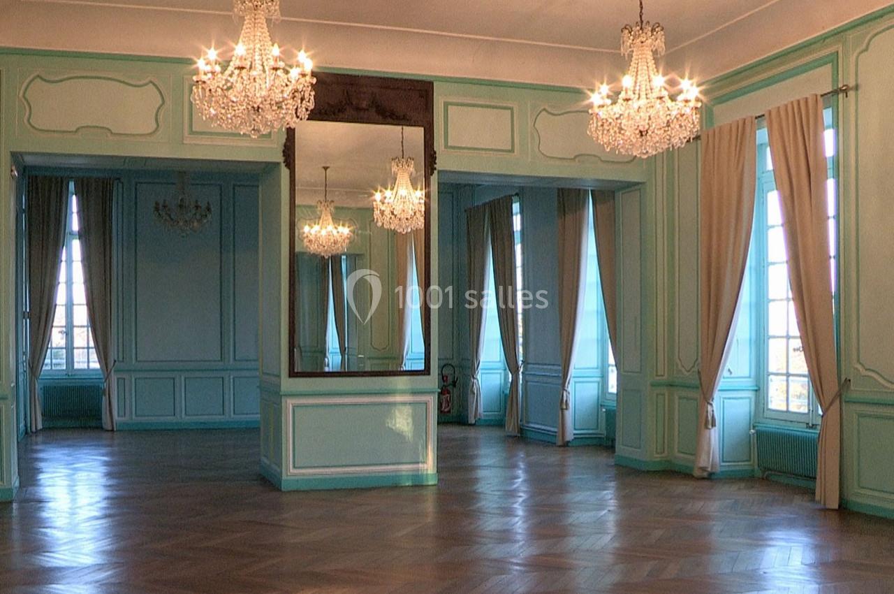 Salle élégante avec parquet en bois, murs bleu pastel, grands miroirs, lustres en cristal et hautes fenêtres avec rideaux.