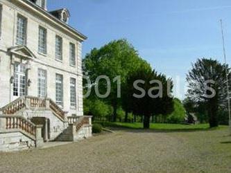 Façade d'un bâtiment ancien en pierre avec escalier, entouré d'arbres et d'une allée gravillonnée.