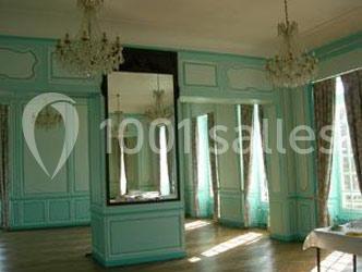 Salle lumineuse avec moulures vert pastel, grands miroirs, lustres suspendus et fenêtres avec rideaux ouverts.