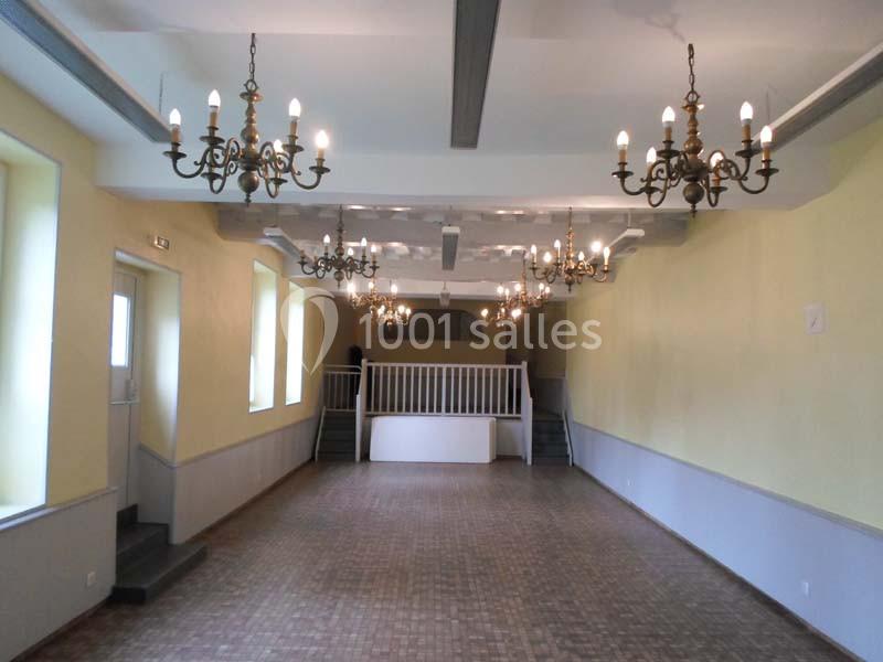 Salle vide avec parquet, murs jaunes, plusieurs lustres suspendus et une estrade au fond avec des escaliers.