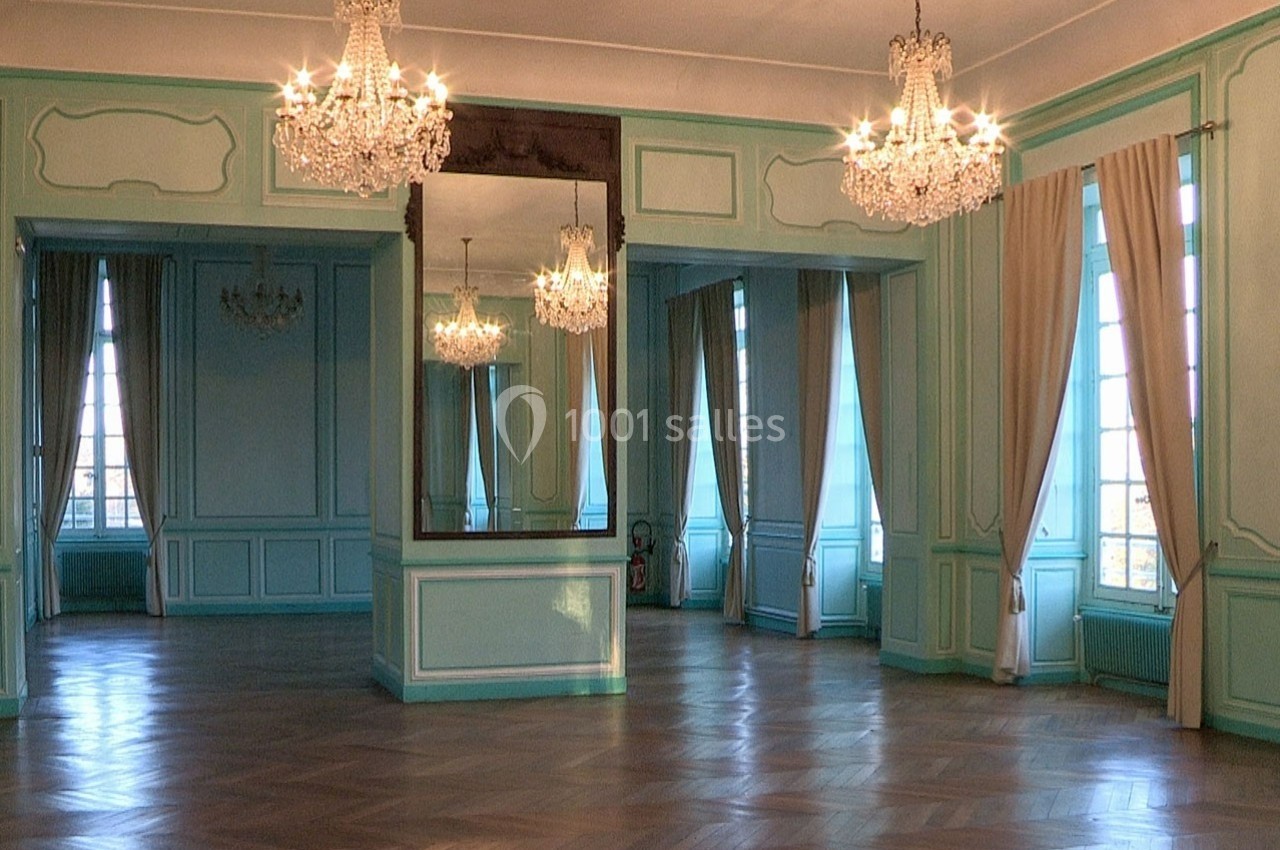 Salle élégante avec parquet en bois, murs bleu clair, miroirs, lustres en cristal et grandes fenêtres avec rideaux beiges.