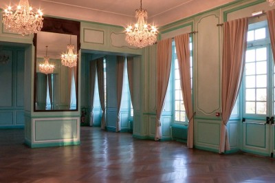 Salle de réception élégante avec tables rondes dressées, chaises blanches et lustres suspendus.