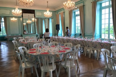 Salle de réception élégante avec tables rondes dressées, chaises blanches et lustres suspendus.