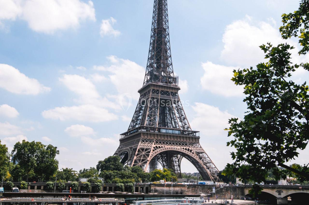 Vue de la tour Eiffel par une journée ensoleillée, avec des bateaux amarrés sur la Seine au premier plan.