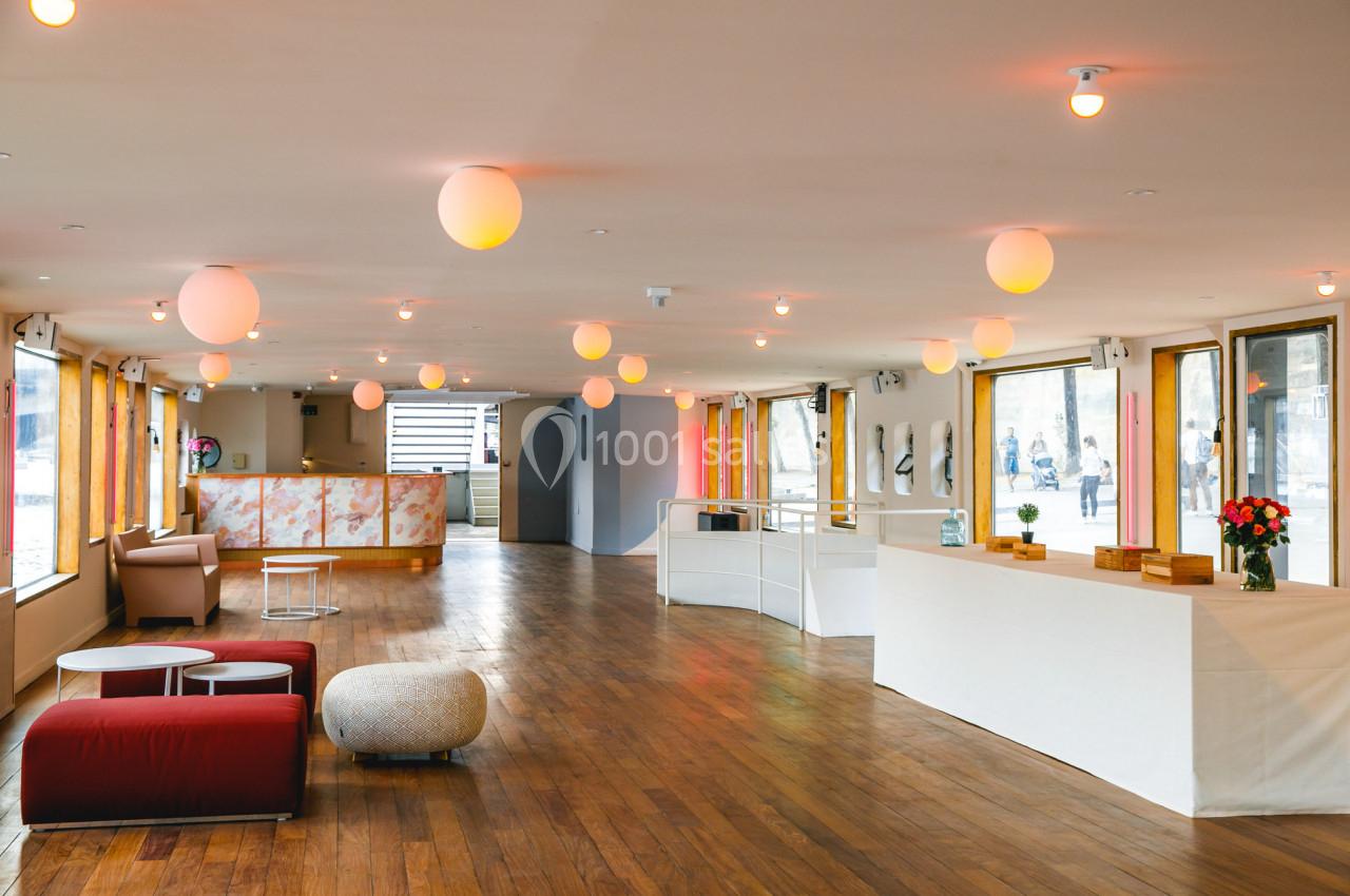 Salle lumineuse avec parquet, mobilier moderne, comptoir blanc et grandes fenêtres laissant entrer la lumière naturelle.