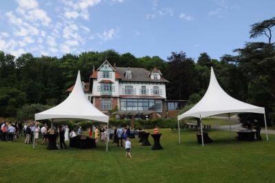 Des lanternes lumineuses flottent dans la nuit près d'une grande maison éclairée en bleu, entourée de personnes.