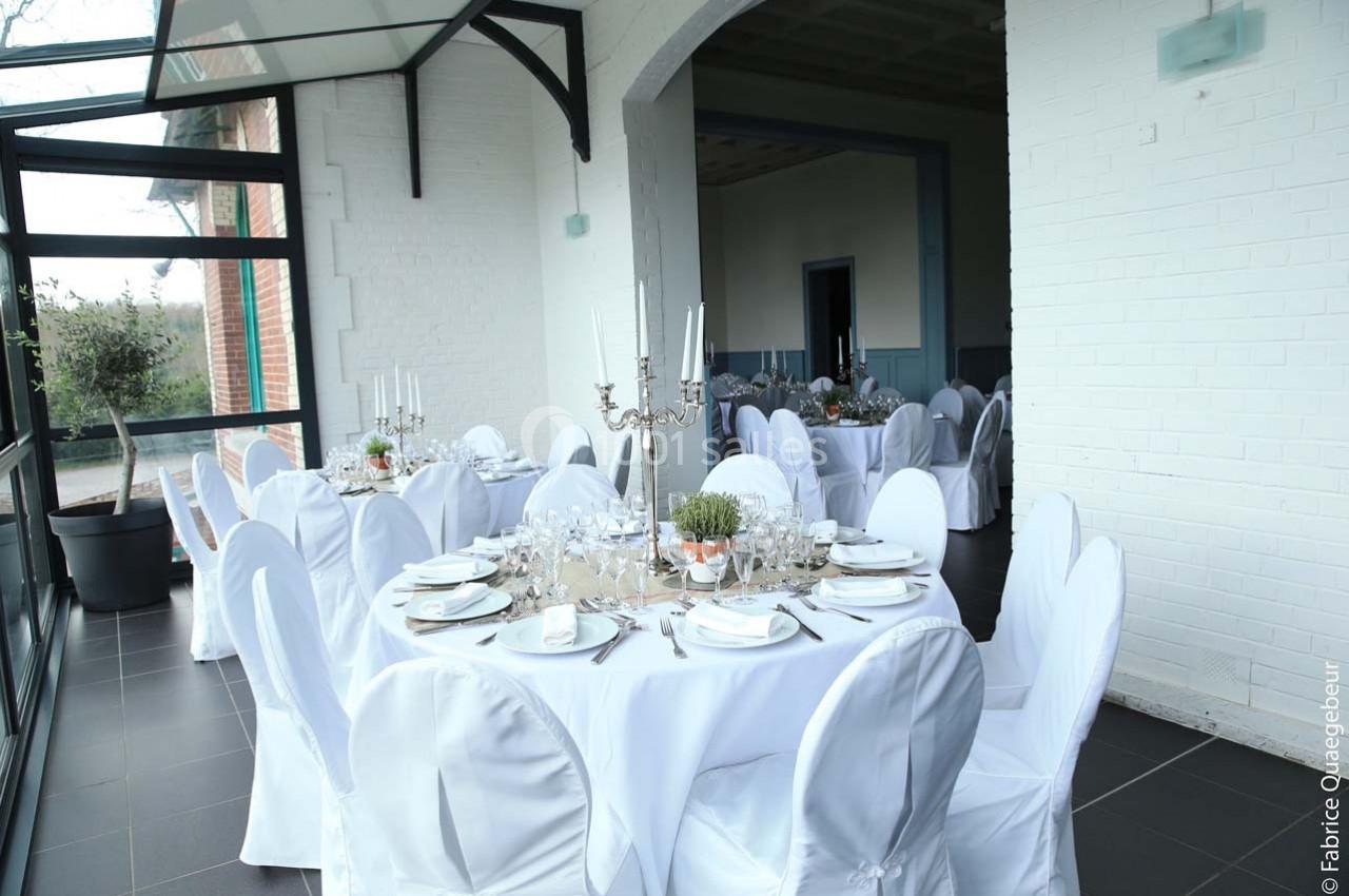 Salle lumineuse avec tables rondes dressées, nappes blanches, chandeliers et baies vitrées donnant sur l'extérieur.