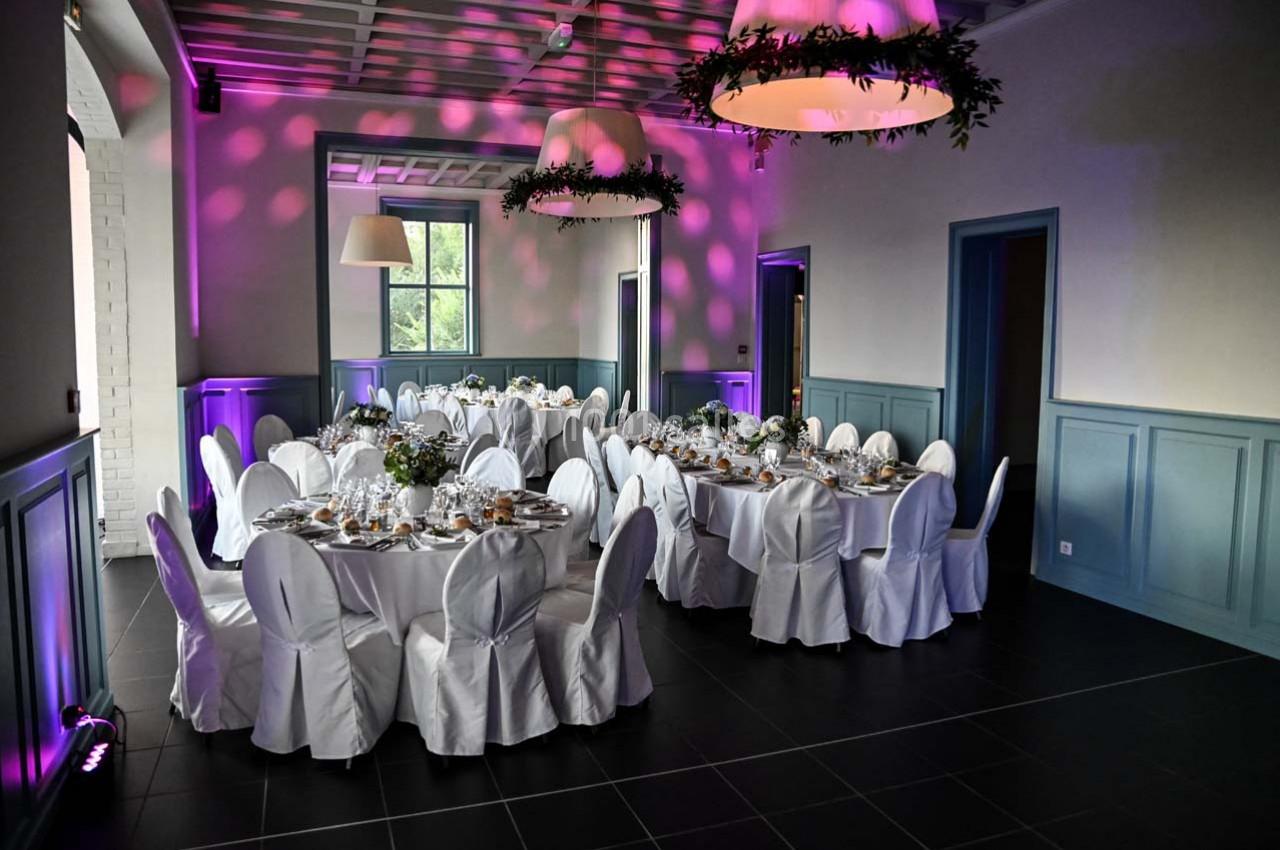 Salle de réception élégante avec tables rondes dressées, nappes blanches et éclairage d'ambiance violet.