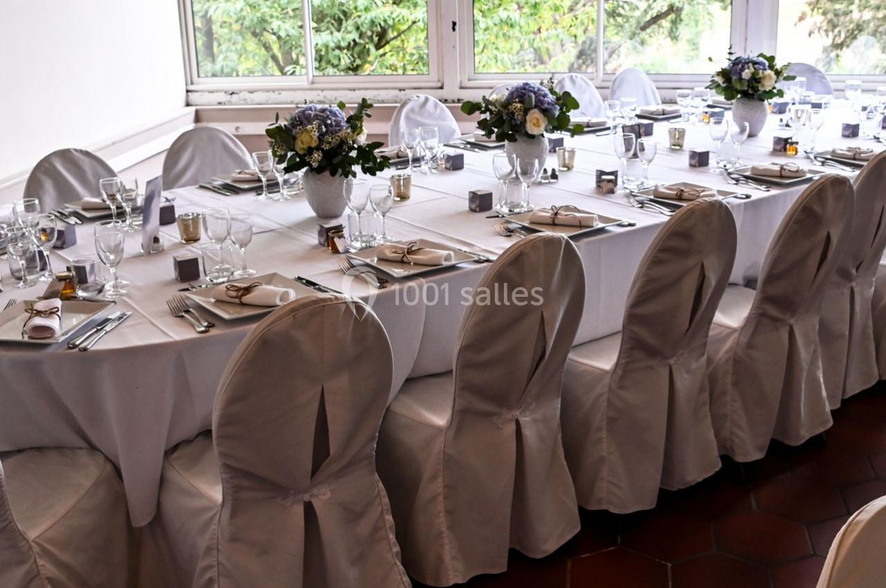 Table élégamment dressée avec nappes blanches, chaises couvertes, vaisselle raffinée et bouquets de fleurs.