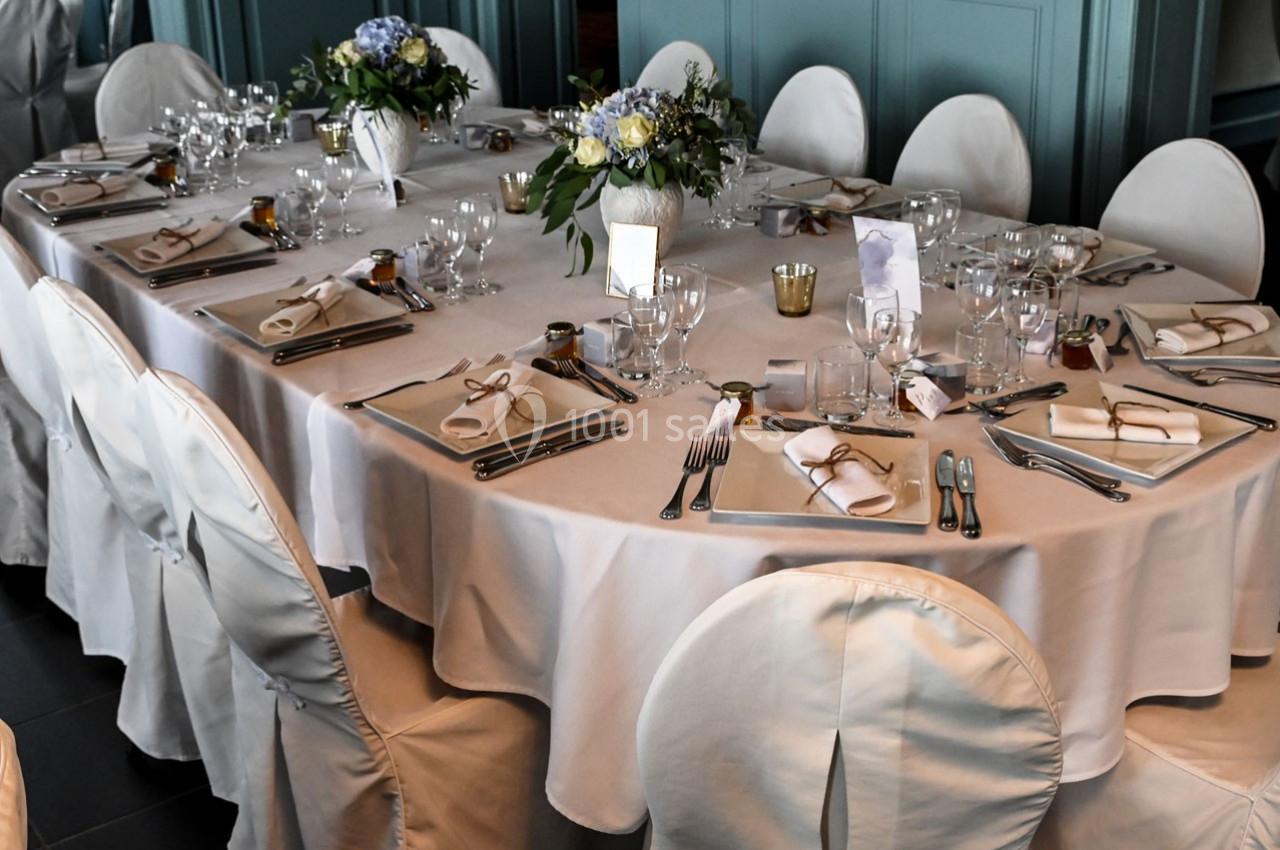 Table élégamment dressée avec nappes blanches, couverts, verres, menus et bouquets de fleurs en centre de table.