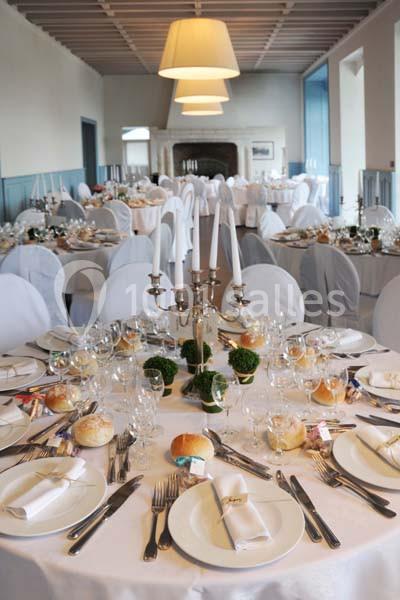 Salle de réception avec tables rondes dressées, nappes blanches, chandeliers et couverts élégants.