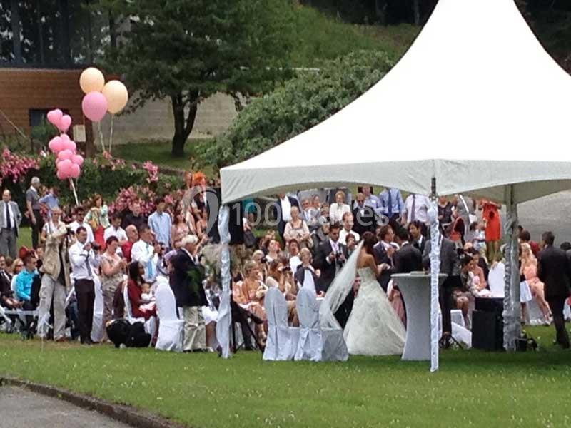 Un mariage en extérieur sous une tente blanche, avec des invités assis et des ballons roses en arrière-plan.