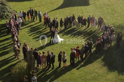 Des lanternes lumineuses flottent dans la nuit près d'une grande maison éclairée en bleu, entourée de personnes.