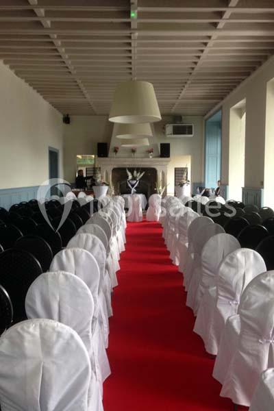 Salle décorée pour un événement avec des chaises couvertes de housses blanches alignées de part et d'autre d'un tapis rouge.