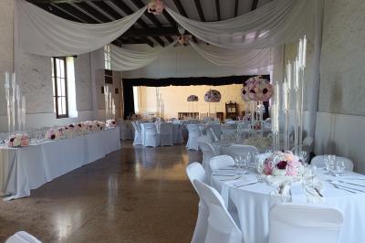 Salle décorée avec des guirlandes roses et blanches, tables dressées pour un buffet sous une charpente en bois.