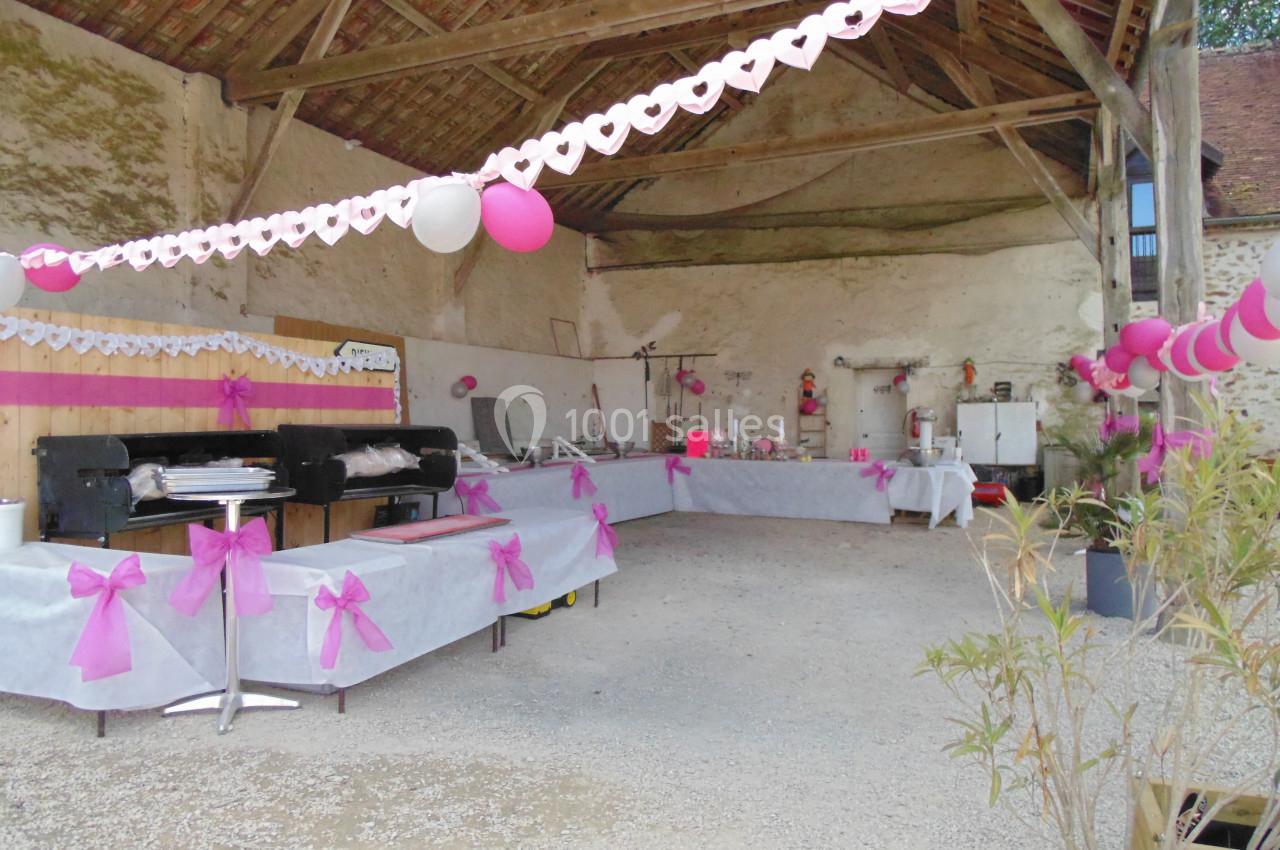 Salle décorée avec des guirlandes roses et blanches, tables dressées pour un buffet sous une charpente en bois.