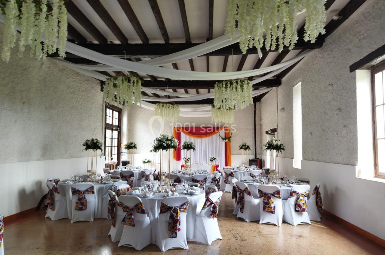 Salle de réception décorée avec des tables rondes, nappes blanches, chaises ornées et guirlandes suspendues.