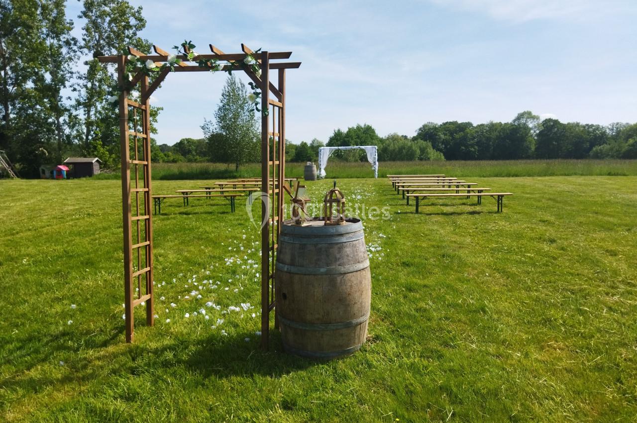Arche en bois décorée, tonneau et bancs disposés sur une pelouse pour une cérémonie en plein air.