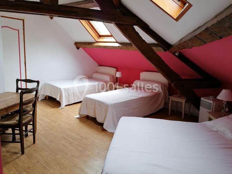 Chambre mansardée avec trois lits simples, poutres apparentes, parquet et murs partiellement peints en rose.